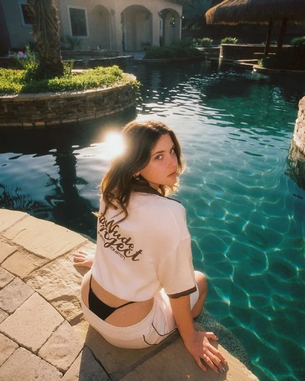 Candid Woman Sitting by Resort Swimming Pool in Vintage Sunlight