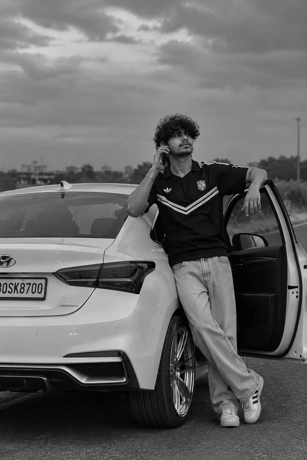 Black and White Portrait of a Young Man on a Phone Leaning on a White Car