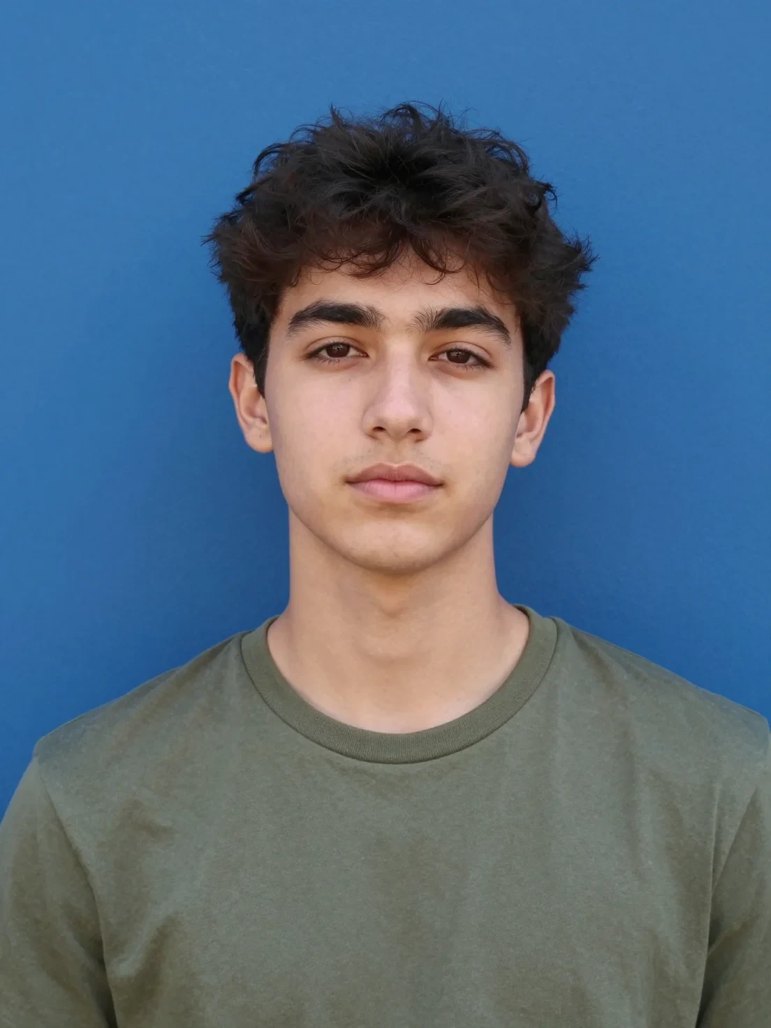 A Young Man with Dark, Textured Hair Poses for a Centered Portrait Against a Flat